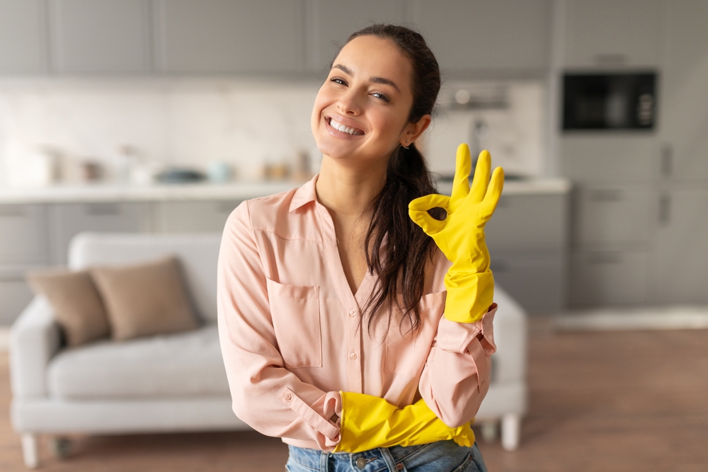 Radiant woman in pink blouse and cleaning gloves making an okay gesture, symbolizing satisfaction with her cleaning in bright kitchen, free space