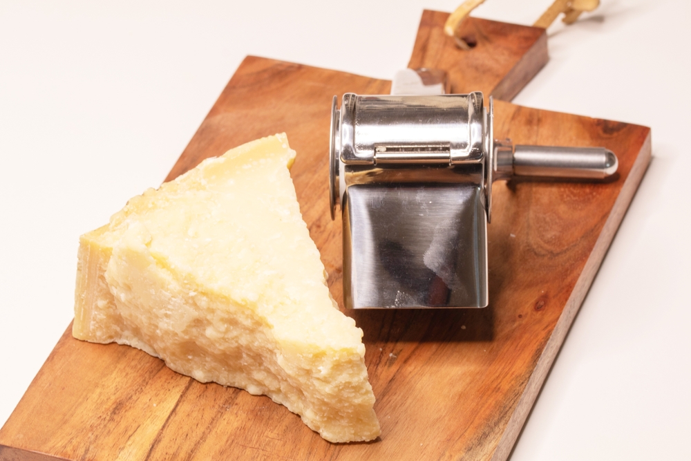 Parmesan cheese on a wooden board with a parmesan grinder
