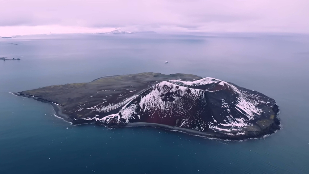 An island in the ocean near Antarctica, featuring a mountainous landscape with clouds in the sky.
