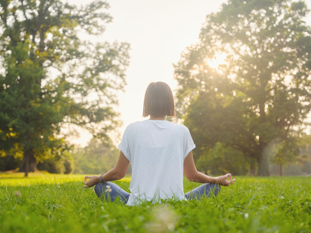 Young asian woman doing meditation in morning or evening at park, healthy woman relaxing and practicing yoga at city park. Mindfulness, destress, Healthy habits and balance concept