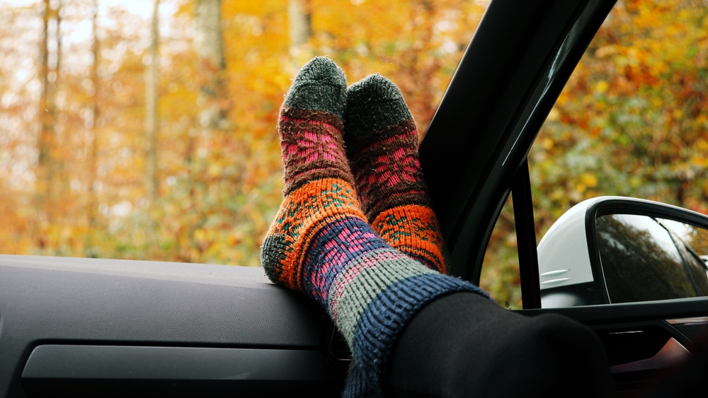 Woman feet in warm colourful socks on car dashboard autumn season. Concept roadtrip freedom.