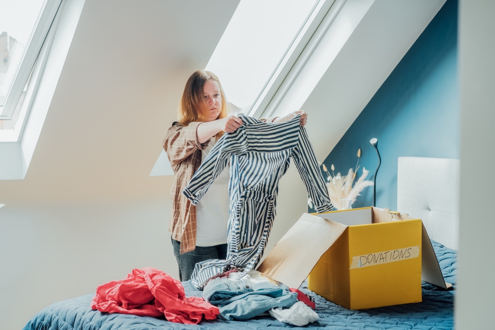 Woman selecting clothes from her wardrobe for recycling, donating to a Charity shop. Decluttering, Sorting clothes, Cleaning Up. Reuse, second hand concept. Conscious consumer, sustainable lifestyle.
