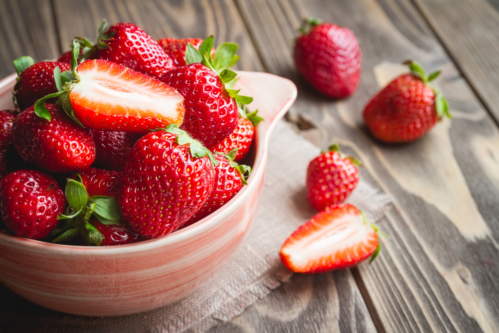 Fresh strawberries in a bowl on wooden table with low key scene.