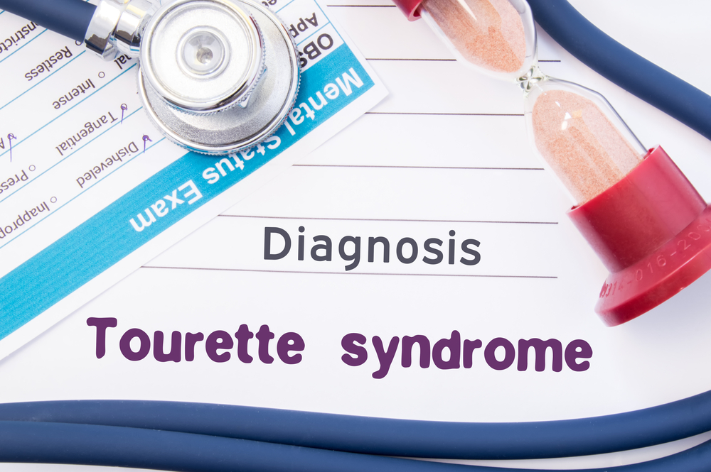 Diagnosis of Tourette syndrome. On psychiatrist or psychologist table is paper with inscription Tourette syndrome (disease) near psychiatric report, hourglass and stethoscope