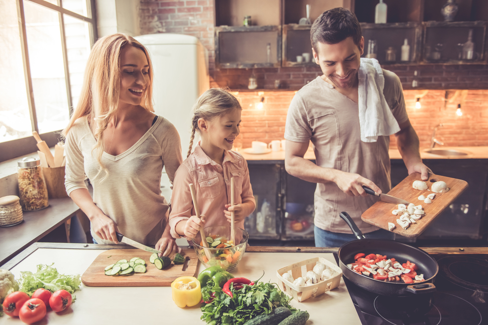 Cute little girl and her beautiful parents are smiling while cooking in kitchen at home
