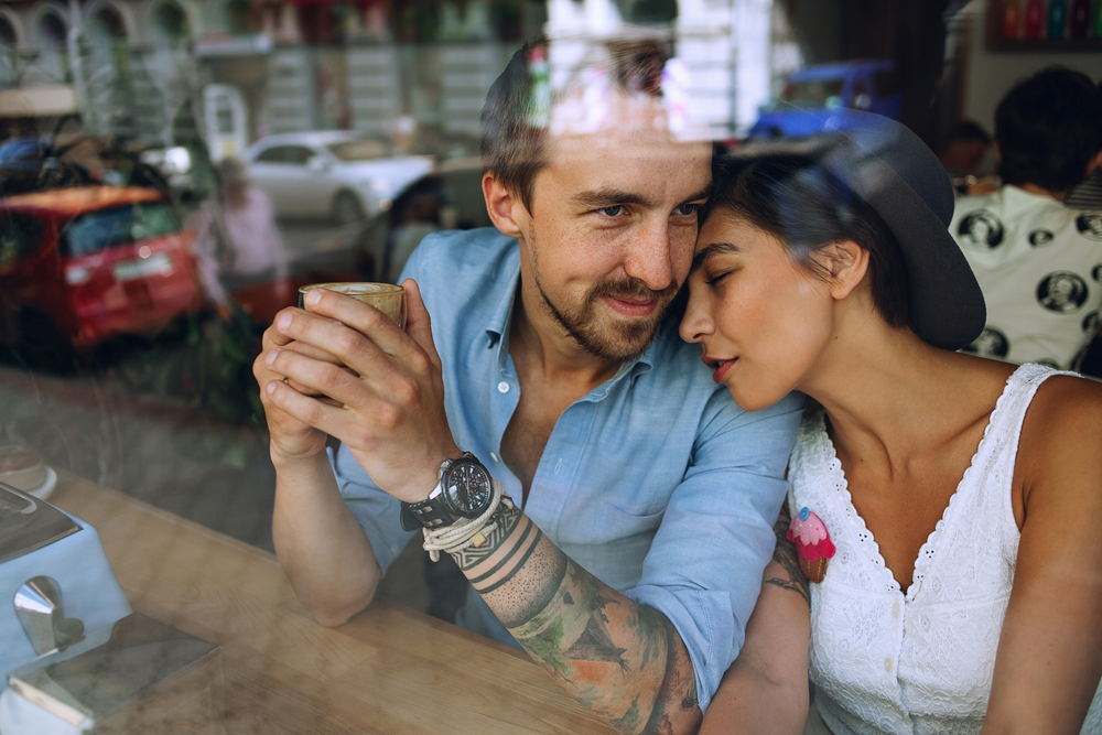 Dreamy couple resting in cafe behind the window at sunny day
