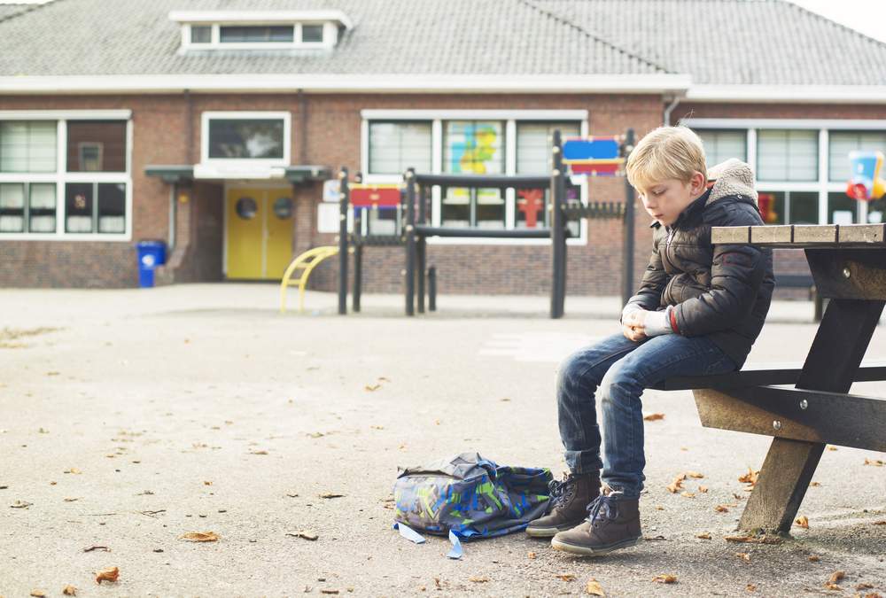 sad boy outside at schoolyard