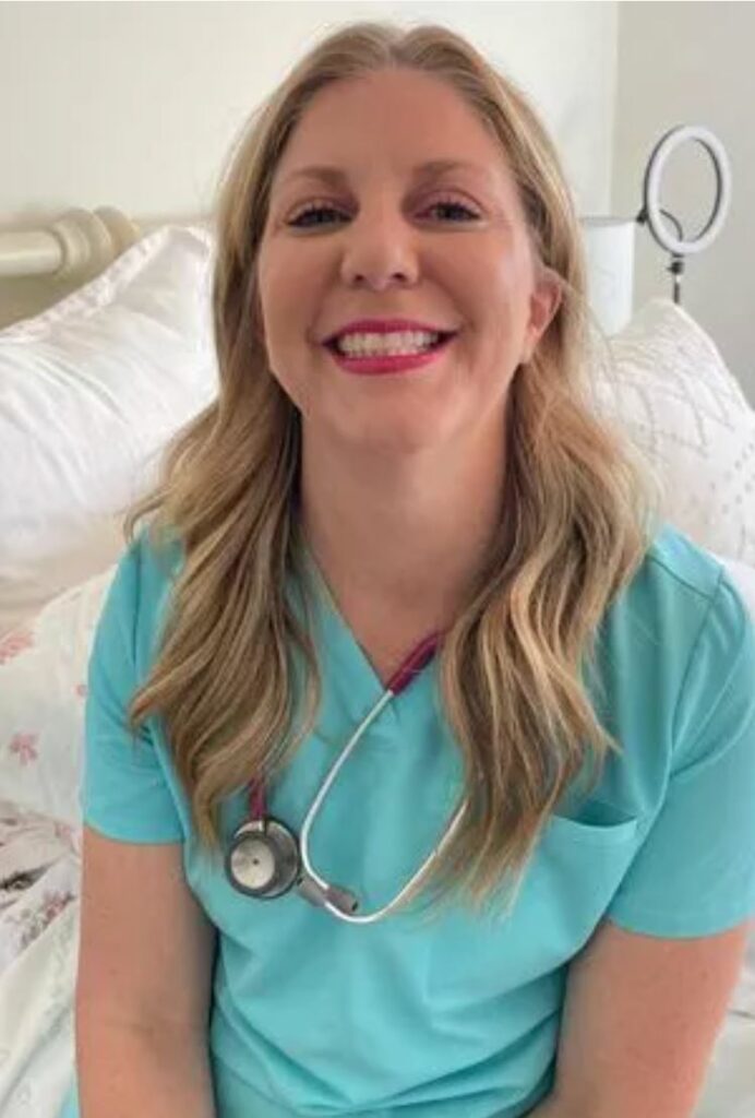 A blonde nurse smiling on a bed. White bedding and walls in the background. 