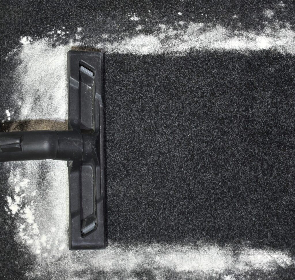 A vacuum going over a charcoal carpet with cleaning powder. 