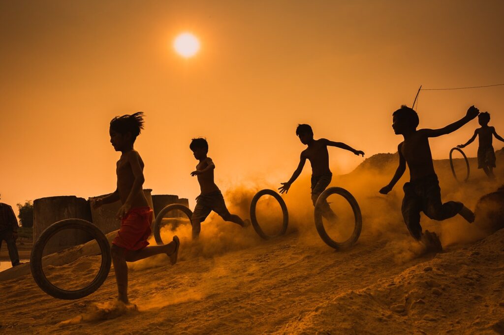 Children running with wheels through sand. Sunset/orange sky in the background.