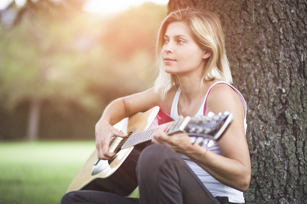 woman sitting under a tree playing guitar