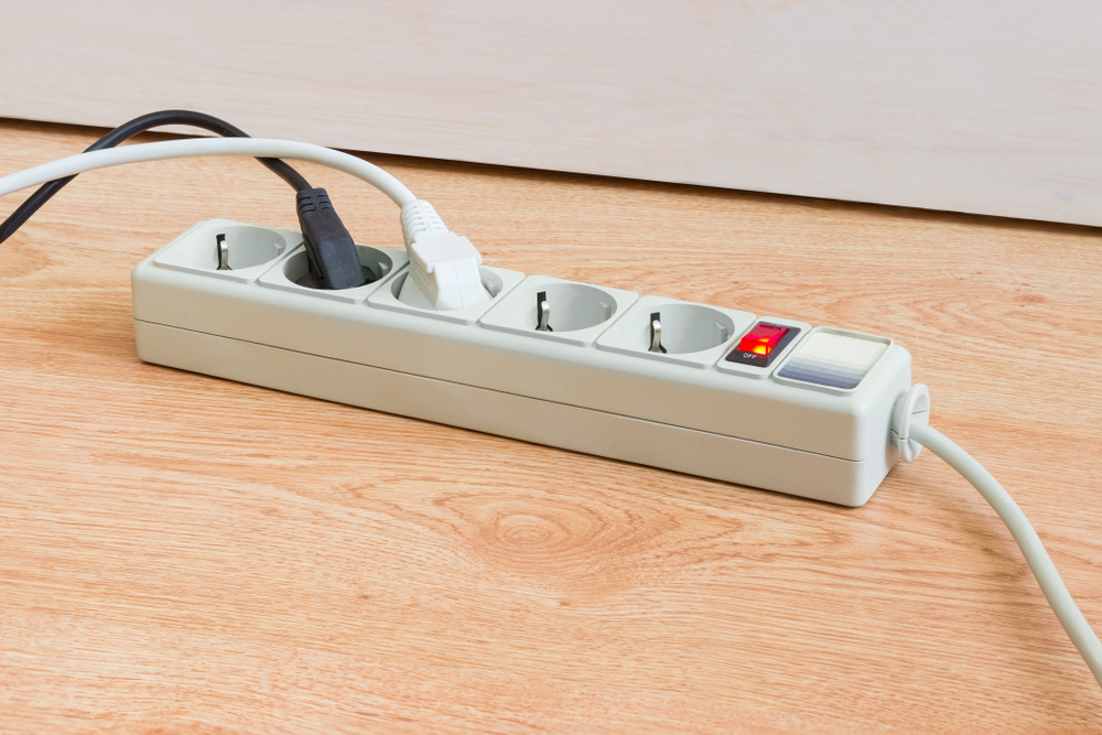 Power strip with electrical sockets of CEE 7 standard, illuminated power circuit breaker and two connected to it power plugs with corresponding mains cables on a wooden surface
