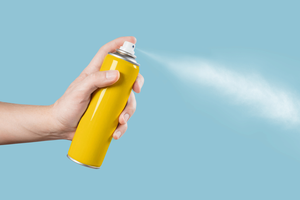 Hand using yellow spray, isolated on blue background