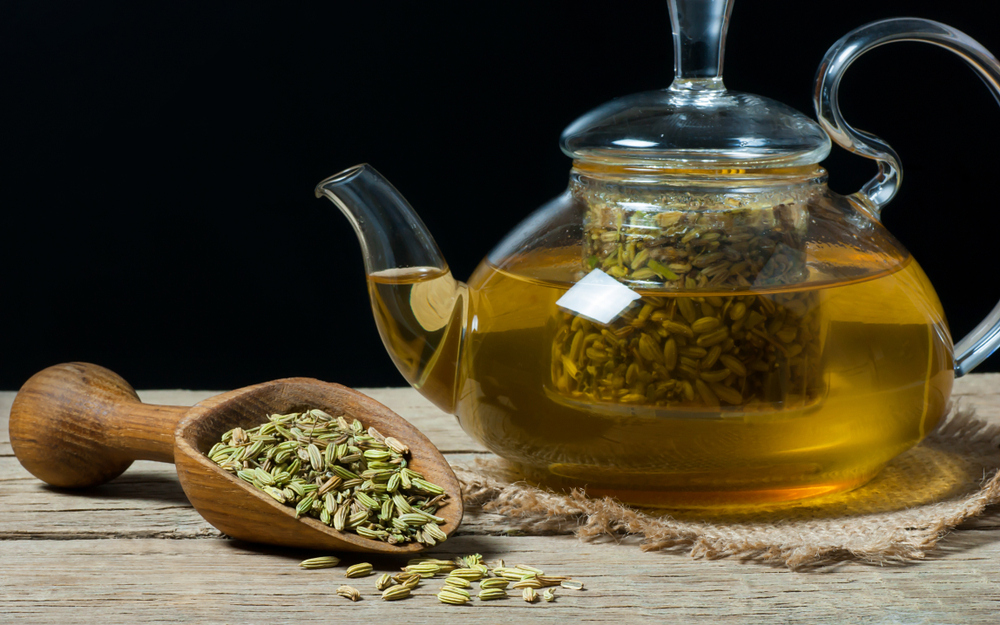 Herbal infusion fennel tea in glass cup with dried fennel seeds in wooden shovel. Herbal tea alternative medicine background concept.
