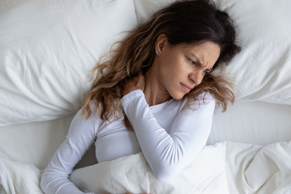 Above view frown millennial woman feels pain in neck after night, awaken in bad temper having painful sudden ache or stiffness, concept of poor incorrect posture during sleeping or too soft mattress
