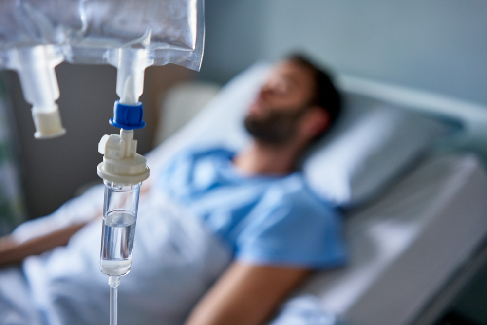 Intravenous drip treatment being used to treat a sick man lying on a bed in a hospital
