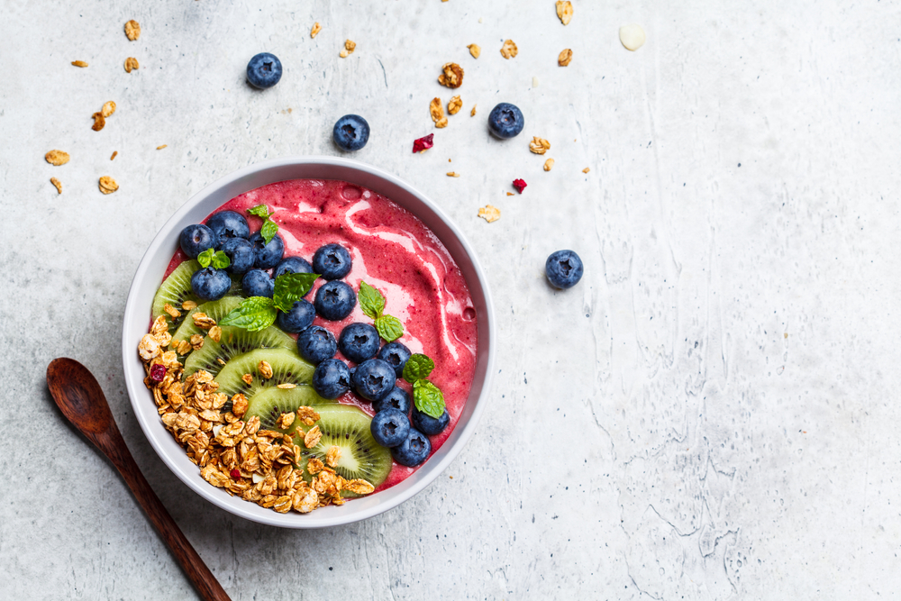 Pink berry smoothie bowl with granola, kiwi and blueberries, light gray background, copy space.