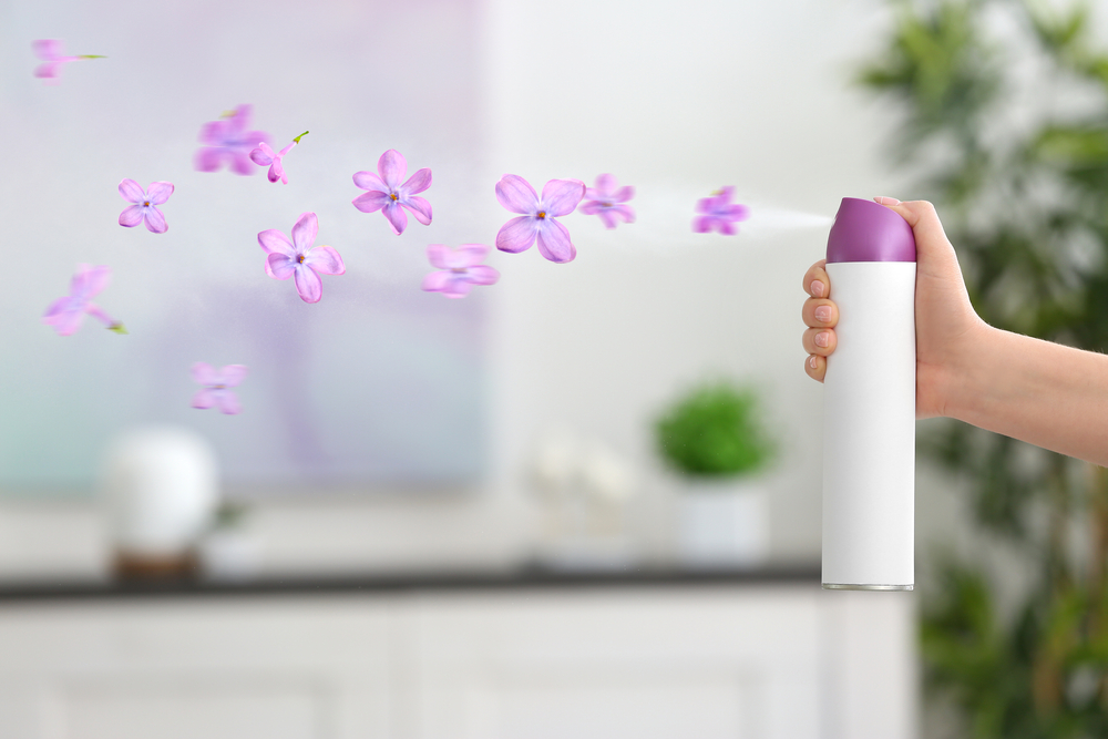 Woman spraying floral air freshener at home