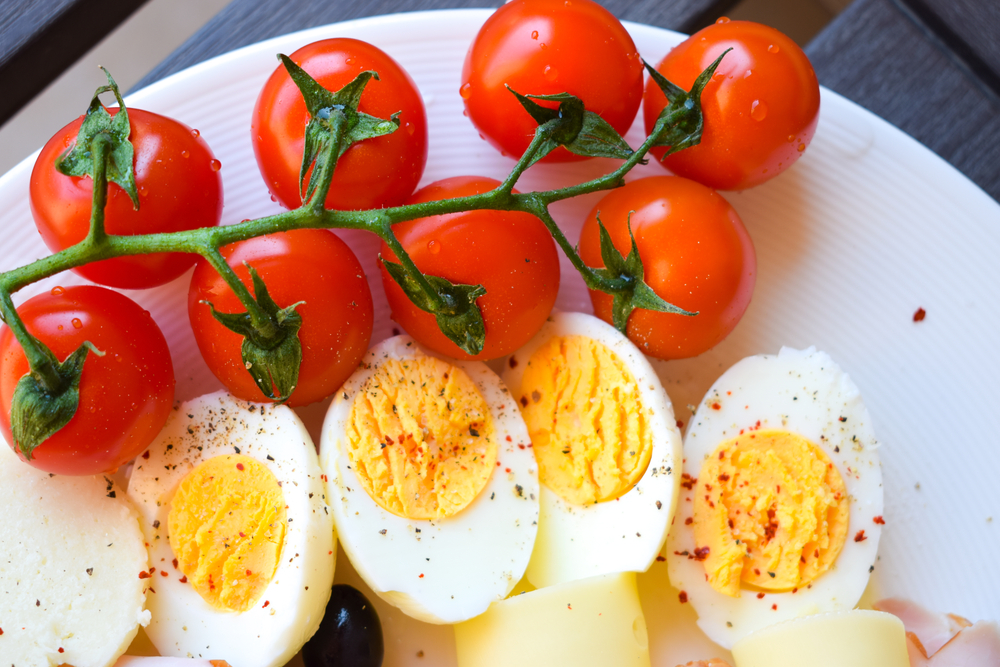 Delicious fresh breakfast plateau with Cherry Tomatoes, Cheese, Cucumber, Ham, Boiled Eggs and Olives. Closeup of tasty breakfast meal. Eating home is healthy.
