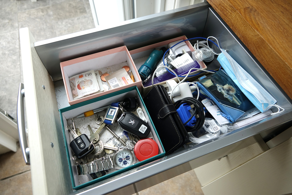 Dartmoor, England. Kitchen drawer with essential items. Car keys, mobile phone, cash and notes, postage stamps. Purse. Phone chargers, face mask. tape measure, House keys, torch, watch.
