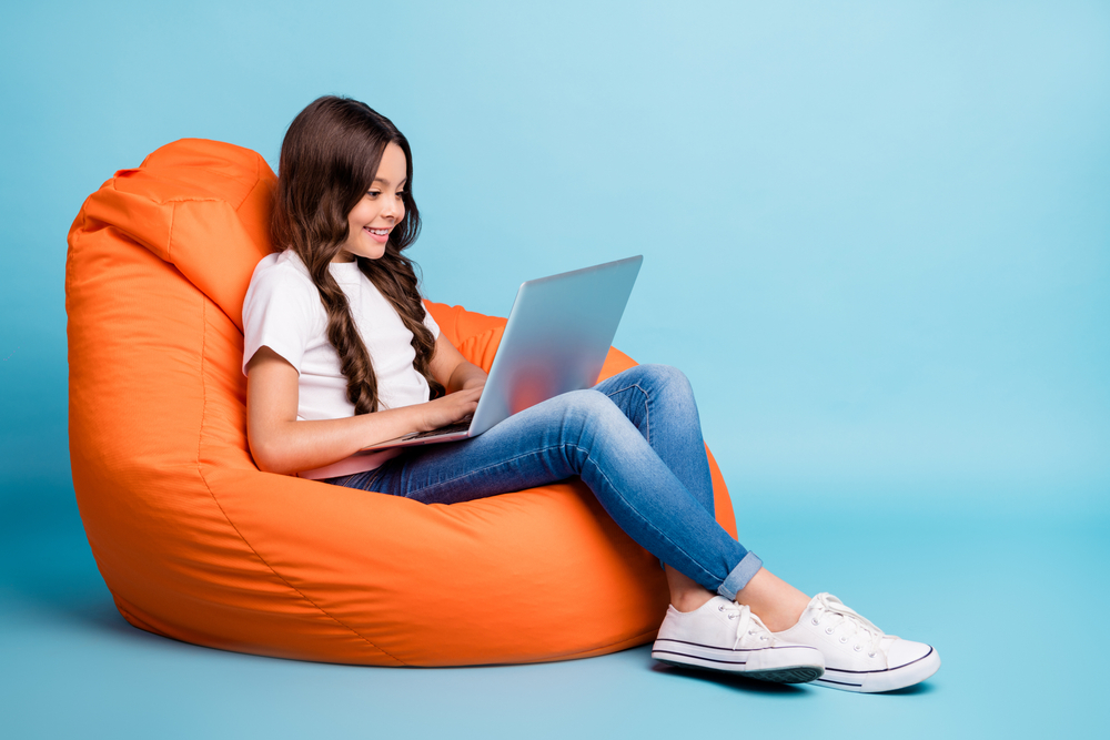 Portrait of nice attractive lovely pretty cute focused cheerful wavy-haired girl sitting in chair using laptop isolated on bright vivid shine vibrant blue teal turquoise color background