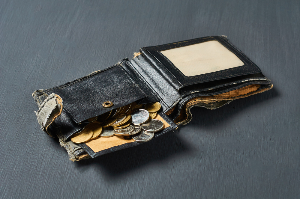 Old battered wallet and lot of coins on concrete desk. Concept of social payments and donations, poverty
