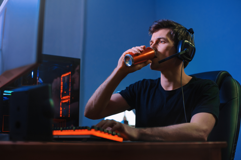 Cyber sport. Professional cybersport player training or playing online video game on his PC late at night, drinking caffeine energy drink to concentrate, focus on game. Team play. Games addiction