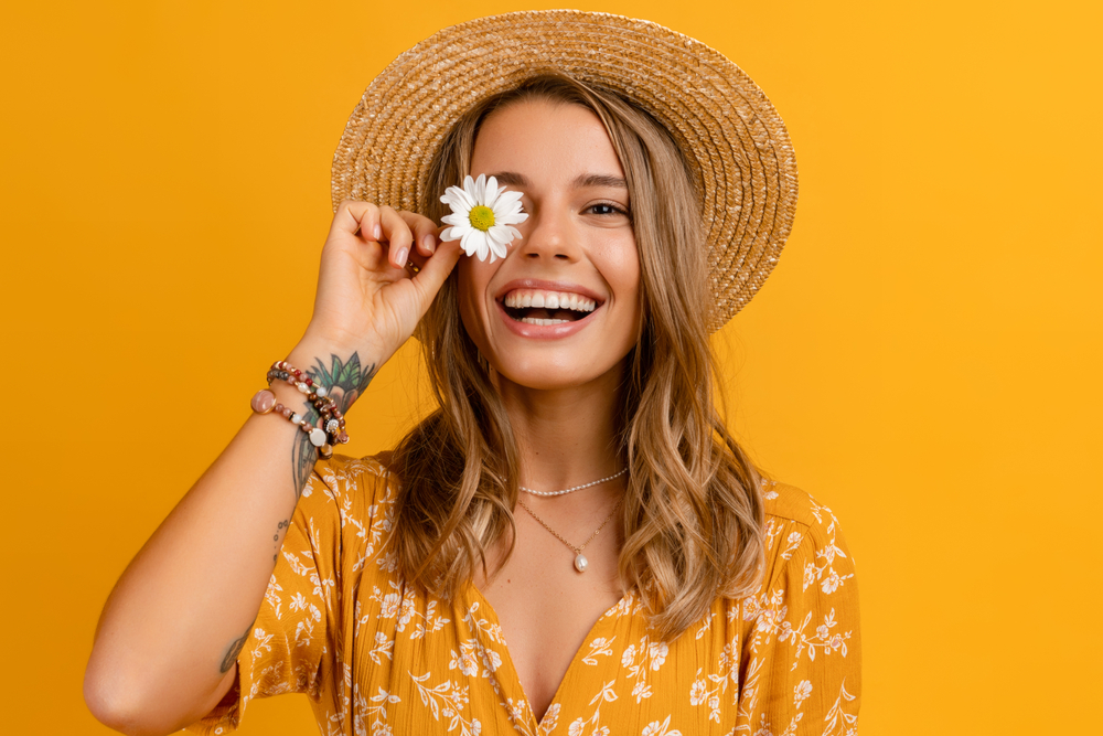 beautiful attractive stylish woman in yellow dress and straw hat holding daisy flower romantic mood posing on yellow background isolated in love summer fashion trend style, natural look
