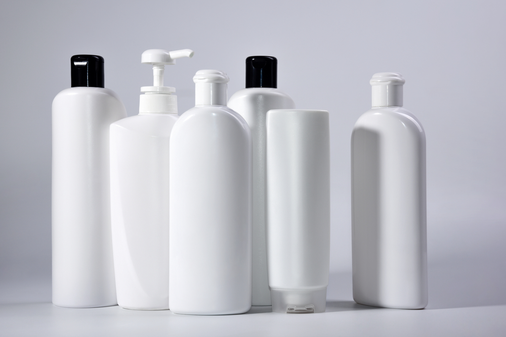 Six white plastic bottles with shampoo and conditioner and shower gel on a white background.
