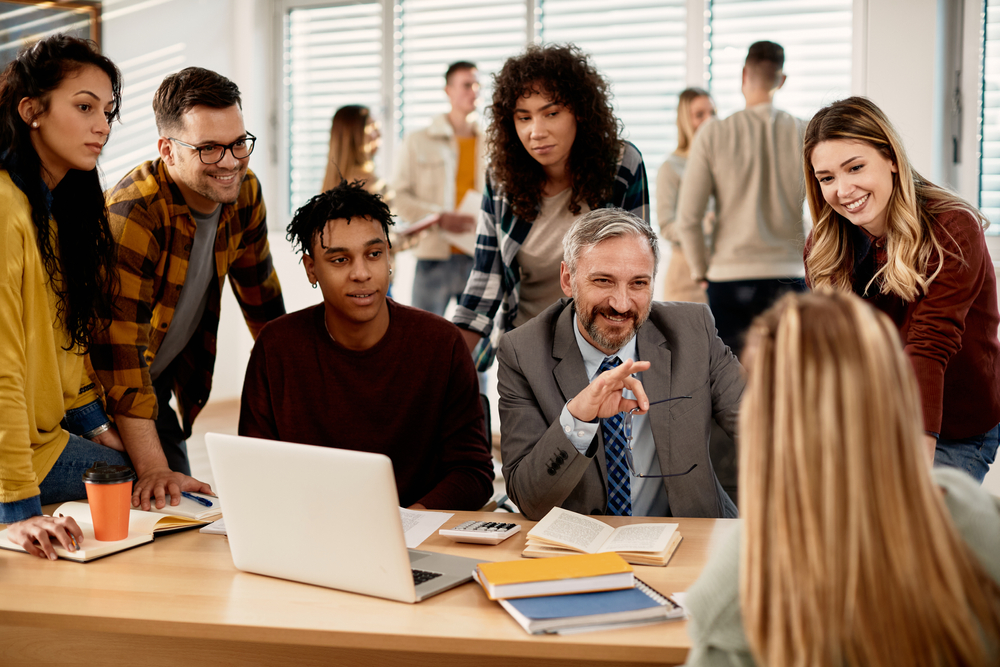 Happy mature professor communicating with group of college students in the classroom.
