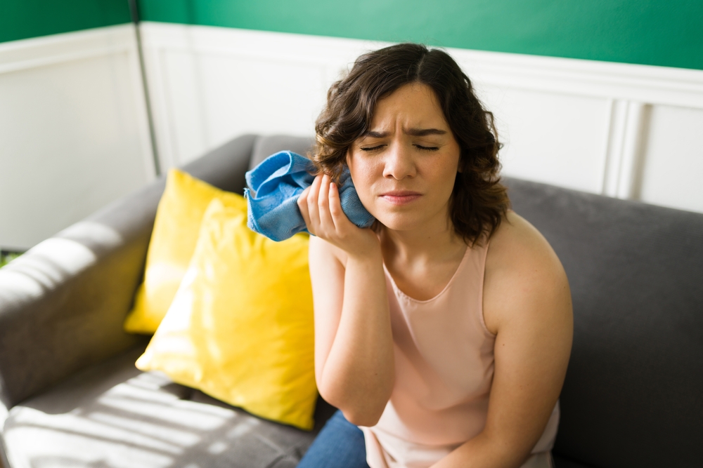 Wisdom teeth. Stressed woman having a lot of pain and putting a compress on her face