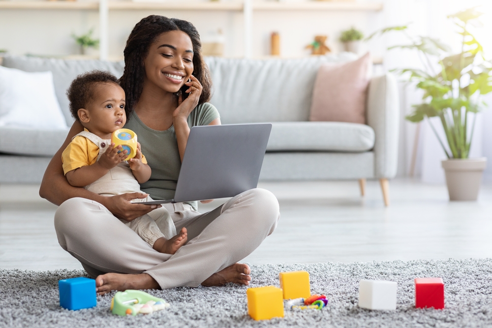Remote Business. Portrait Of Happy Black Woman With Baby Working With Laptop And Cellphone At Home, Busy Young African American Lady Using Laptop And Mobile Phone For Online Work, Copy Space