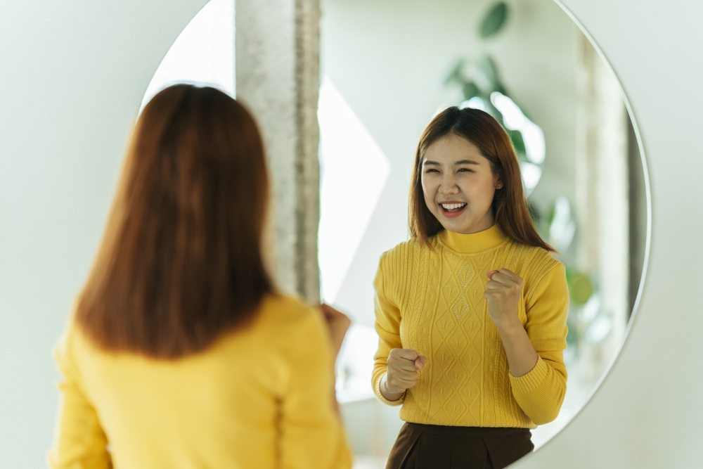 A young Asian woman talks to herself through a mirror to build her self-confidence and empower herself.