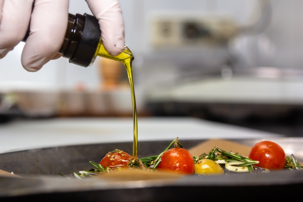 Food concept. Chef is pouring olive oil over fresh salad in restaurant kitchen.