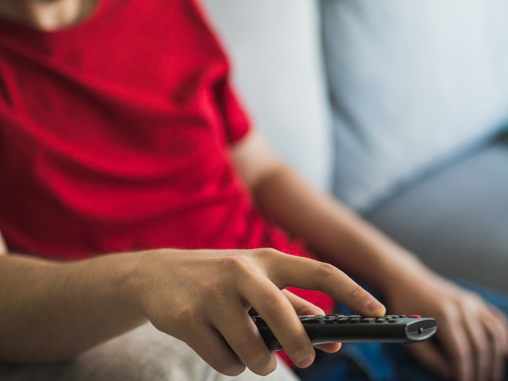 Sedentary man with red t-shirt changing television channel with the remote control. sedentary life concept