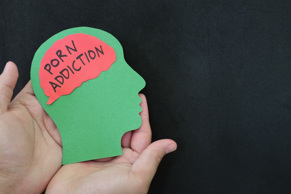 Porn addiction treatment and how to deal with concept. Hand holding human head profile with pornography word on brain.