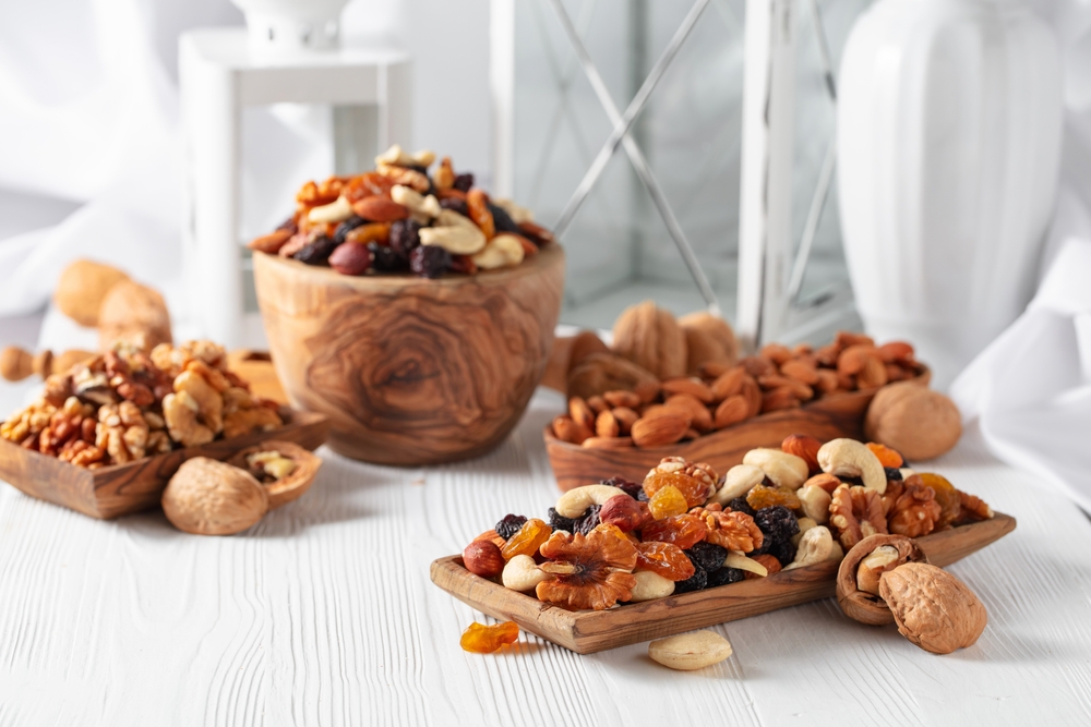 Mix of nuts and raisins on a white wooden table. Presented raisins, walnuts, hazelnuts, cashews, pecans, and almonds.
