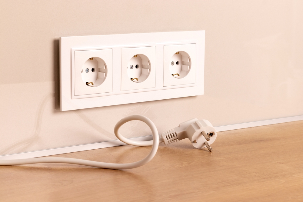 Power cord cable unplugged with group of white european electrical outlets on modern beige wall
