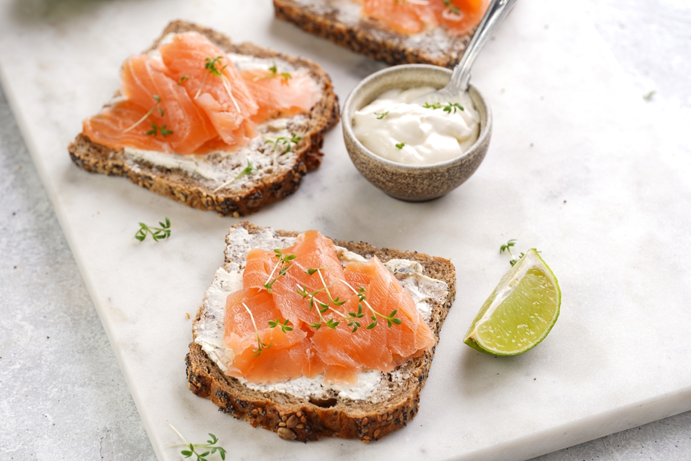Wholewheat bread sandwiches with cream cheese and smoked salmon on marble board with lime slices and sour cream
