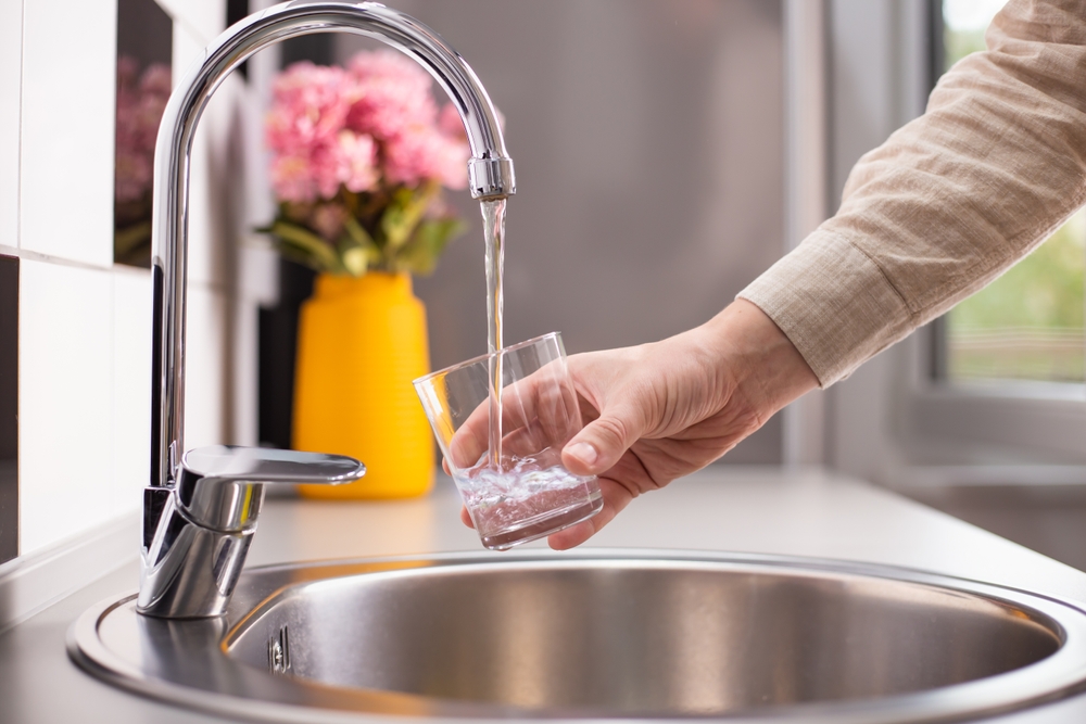 Close up of a man hand filling a glass of water directly from the tap. Filling glass of water from the tap at home.