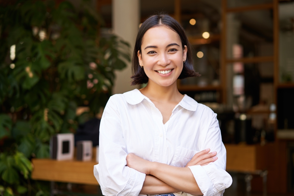 Portrait of smiling asian girl in white collar shirt, working in cafe, managing restaurant, looking confident and stylish.