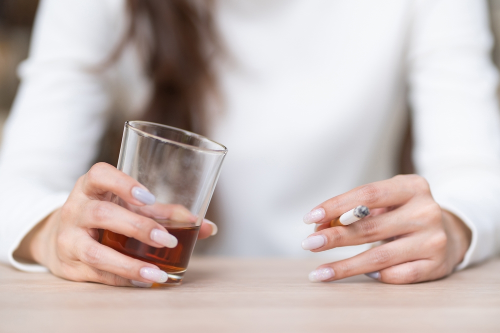 Depressed woman hands drinking alcohol and smoking cigarette lonely.