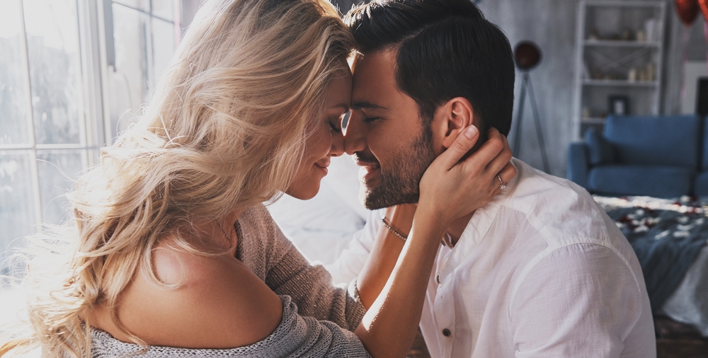 Young loving couple embracing and touching noses while sitting face to face indoor