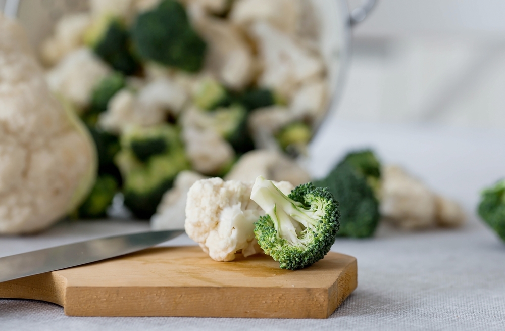 Fresh green broccoli and cauliflower on a wooden chopping board on a linen tablecloth. Broccoli cabbage leaves. Light background. Vegetarian food. Healthy lifestyle.

