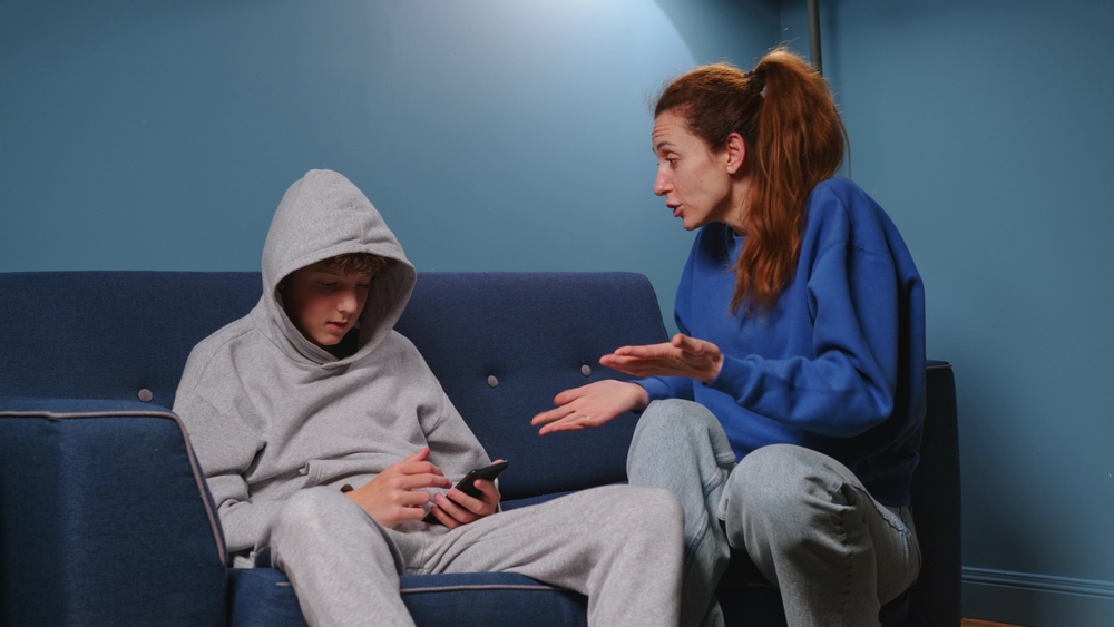 Mom screams and scolds her son in the room on the blue sofa. Irritated woman teaches a lesson to a teenager. The boy has a difficult adolescen