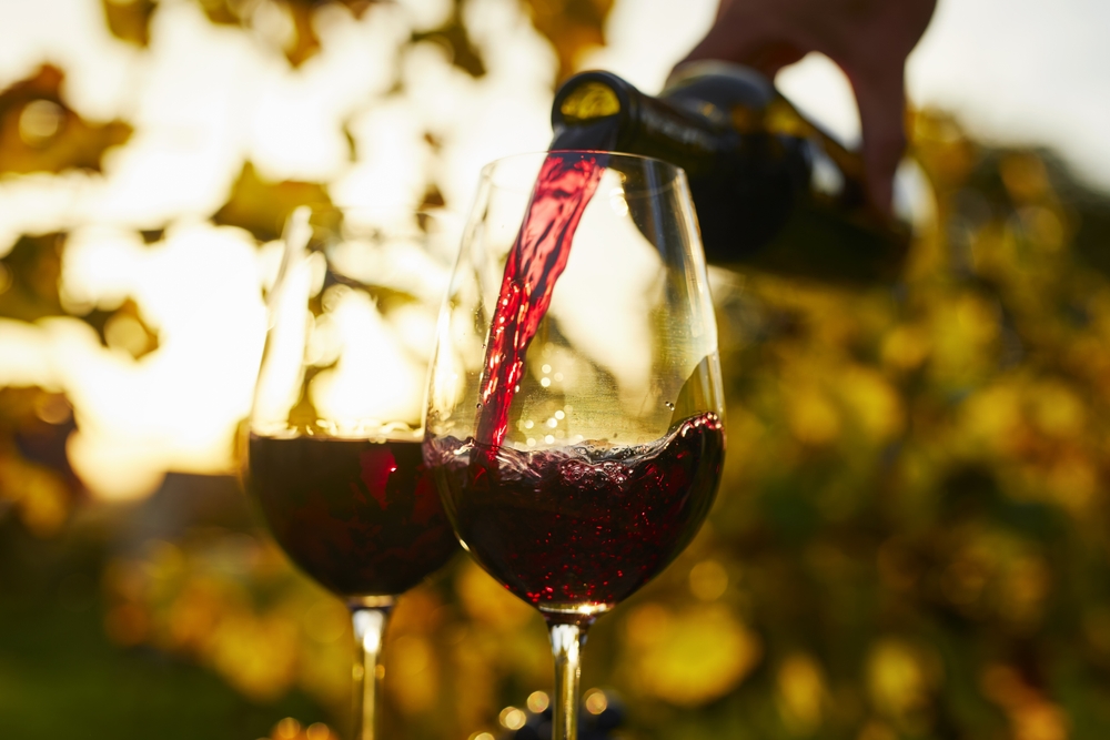 Pouring red wine into glasses at sunset
