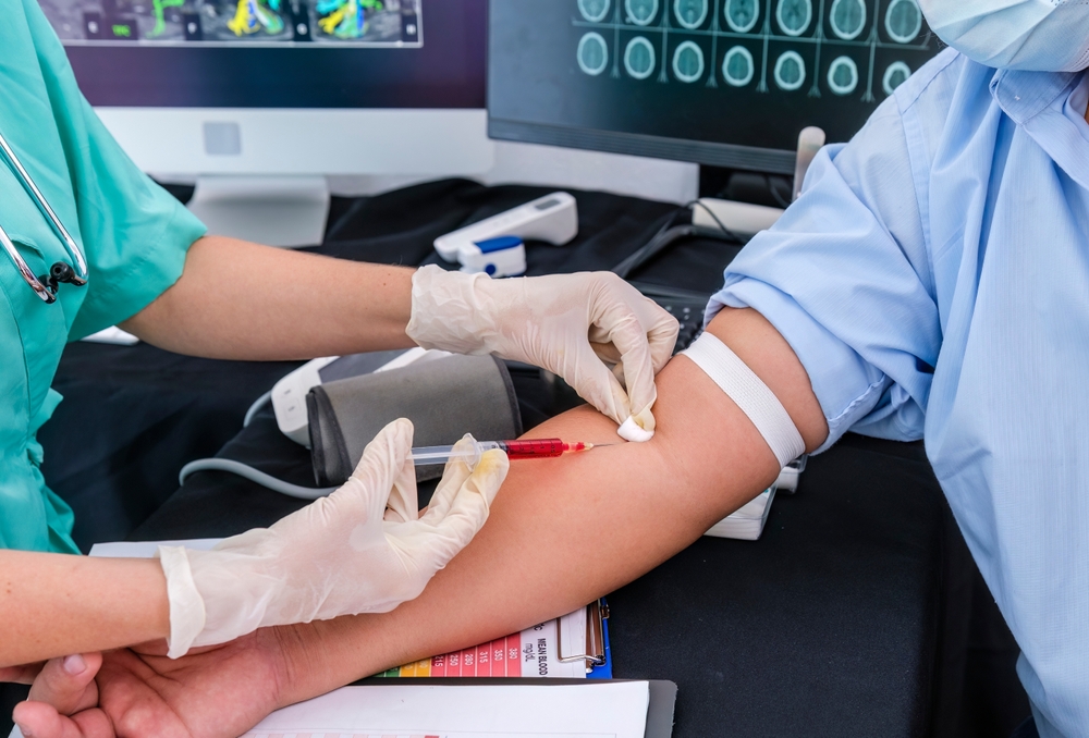 Woman doctor is taking blood example using a syringe to draw blood from the patient's arm.