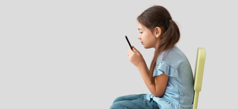 Little girl with bad posture using mobile phone on light background