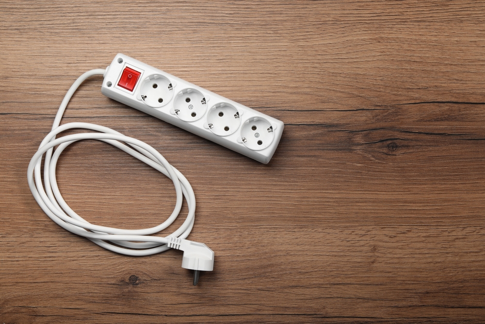 Power strip with extension cord on wooden floor, top view. Space for text
