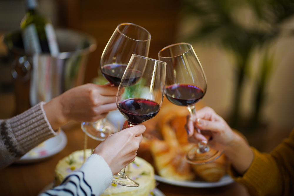 Cheerful friends enjoying home Birthday holiday party. Asian Friends cheering drinking red wine celebrating Christmas or New Year party.
